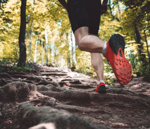 Person trail running on a rocky forest path wearing orange shoes.